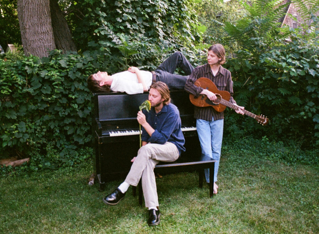 The three members of the Band Bonny Doon in a garden around a piano